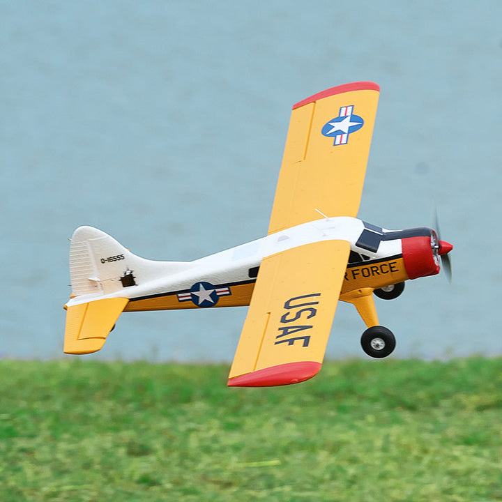 Yellow and white USAF RC trainer airplane flying over a grass field.