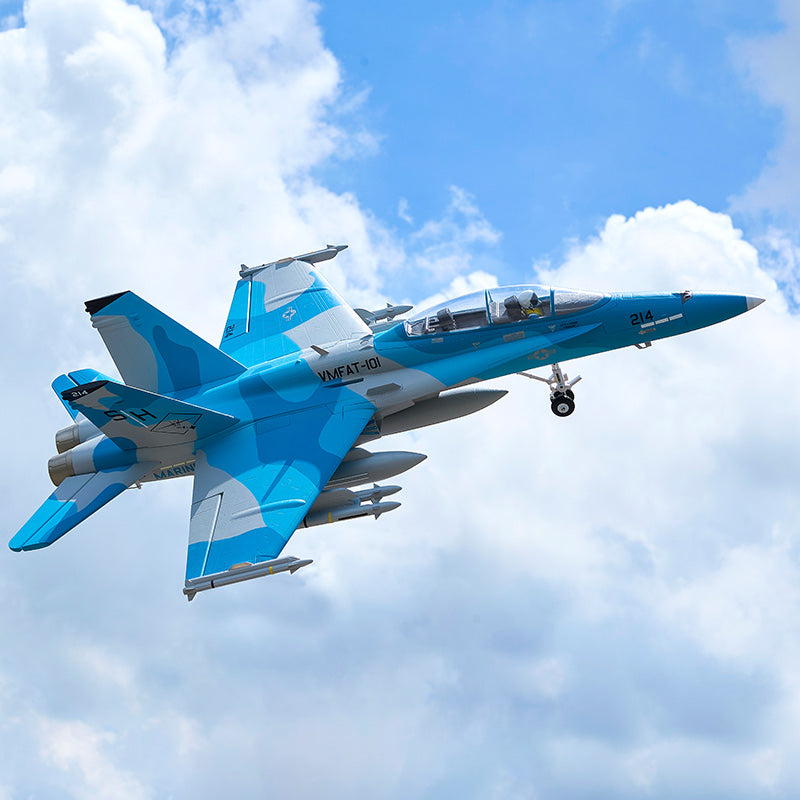 Blue and gray FMS F/A-18 Hornet EDF jet with VMFAT-101 markings in flight against a cloudy sky.