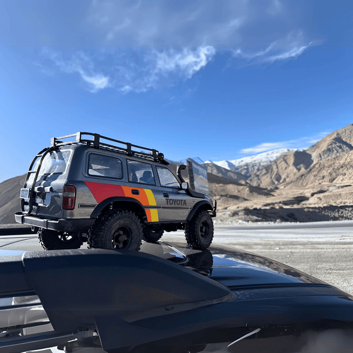 FMS 1:10 FCX10 LC80 Toyota Land Cruiser 80 RS RC car, gray with red-yellow-orange stripes, on roof rack