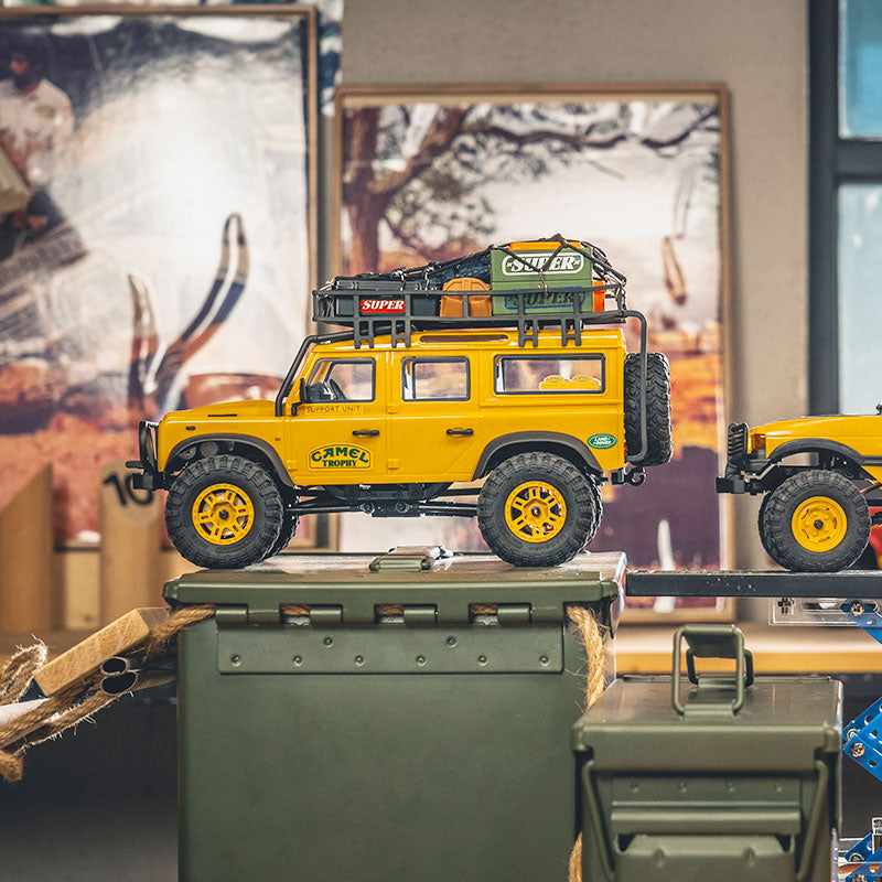 Yellow FMS 1:24 FCX24M Land Rover Camel Trophy RC crawler, loaded roof rack, 'Camel Trophy' decal.