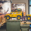 Yellow FMS 1:24 FCX24M Land Rover Camel Trophy RC crawler, loaded roof rack, 'Camel Trophy' decal.