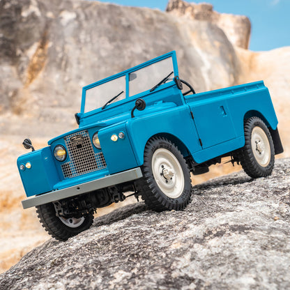 Blue FMS 1:12 Land Rover Series II RTR model off-roading on rocky terrain.