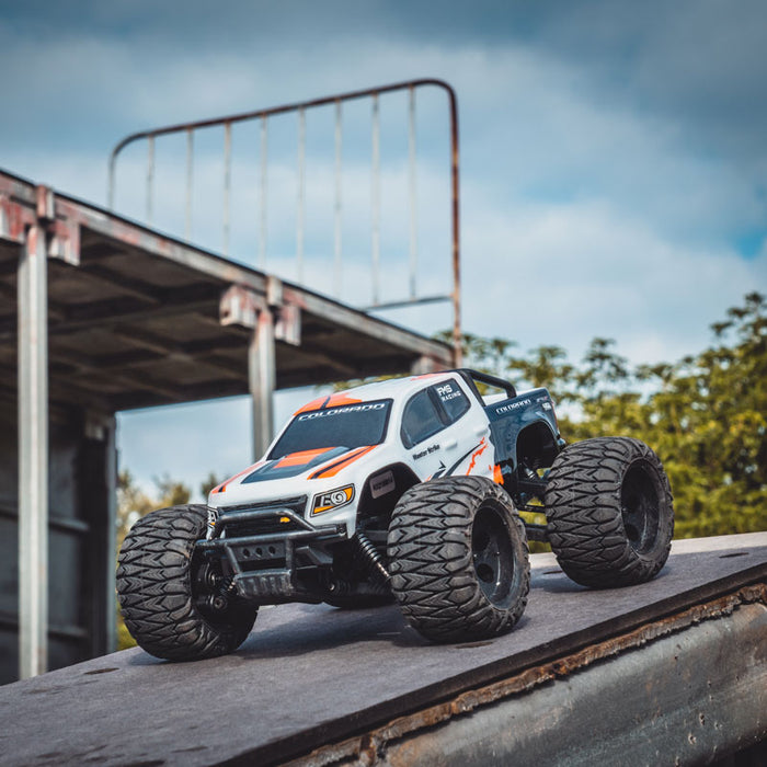 FMS 1:24 FMT24 Chevrolet Colorado monster truck RTR, white with orange accents, large tires, on a ramp.