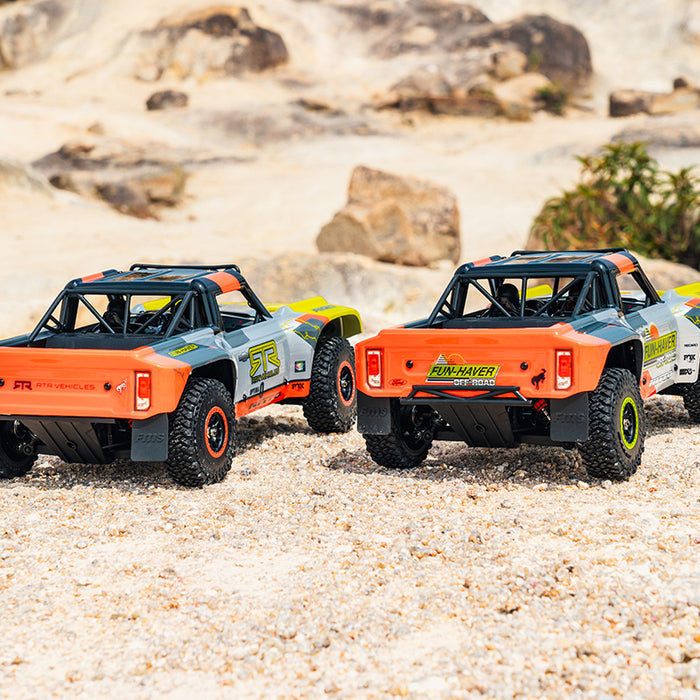 Two FMS 1:18 Ford Bronco RTR RC trucks with orange and grey bodies on sand.