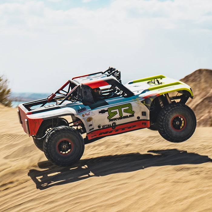 FMS 1:7 Ford Bronco RTR EB Brushless 4WD RS RC truck mid-air jump. White, red, green graphics; "RTR VEHICLE", "NITTO" branding. Off-road.