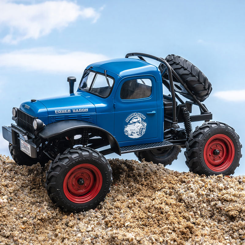 Blue FMS 1:24 scale Power Wagon RC crawler with red wheels and spare tire on sand.