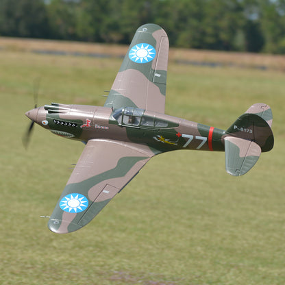 FMS 1400mm P-40B Warhawk Flying Tiger PNP RC plane in flight with camouflage paint, shark teeth nose art, and '77' marking.