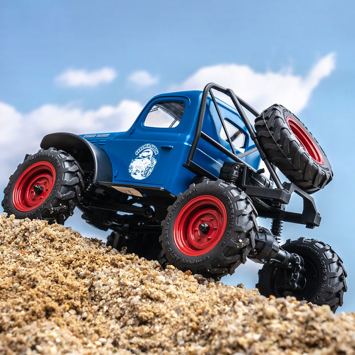 FMS 1:24 FCX24 Power Wagon RTR climbing a sandy hill, blue body with red wheels.