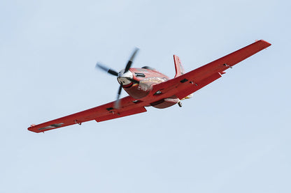 Red FMS 1100mm P-51 Mustang V2 PNP model airplane in flight, with detailed markings and a four-bladed propeller.
