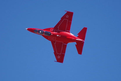 Red FMS 70mm Yak-130 V2 EDF jet in flight against a clear blue sky, showcasing its detailed scale features.