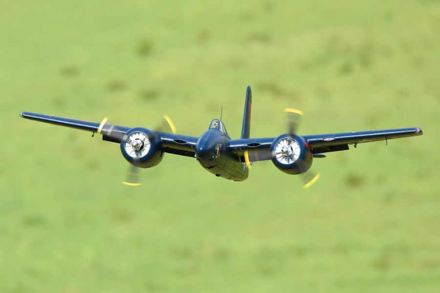 FMS 1700mm F7F Tigercat blue PNP RC aircraft flying against a blurred green background with spinning propellers.